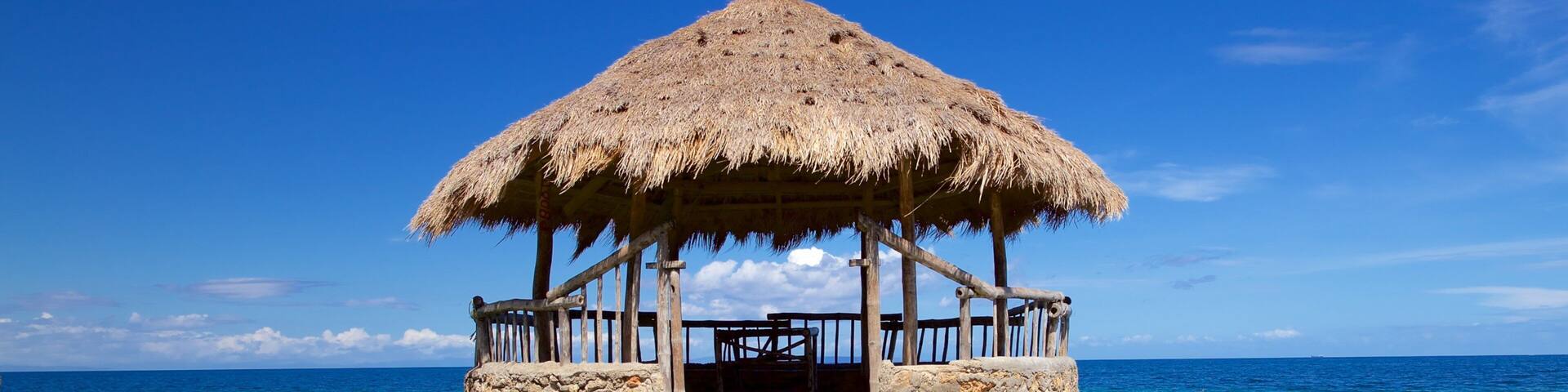 A thatched-roof hut on a stone pier extending into the ocean.