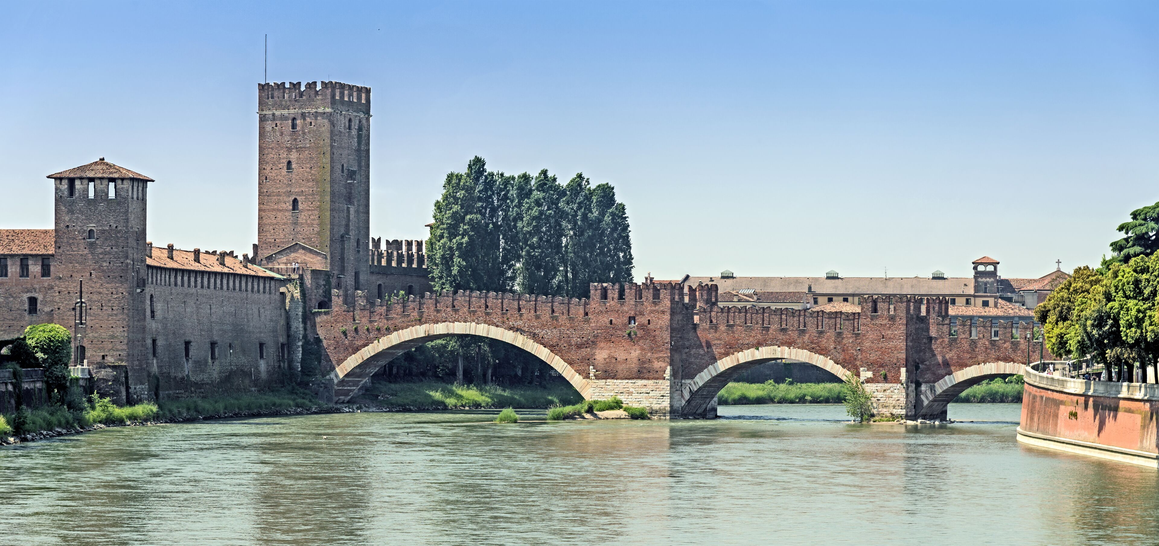Un pont de pierre historique enjambant une rivière, une haute tour et un mur fortifié agrémenté de ponts en arc.