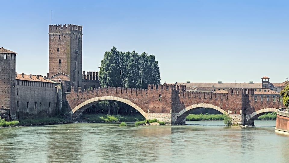 Un pont de pierre historique enjambant une rivière, une haute tour et un mur fortifié agrémenté de ponts en arc.