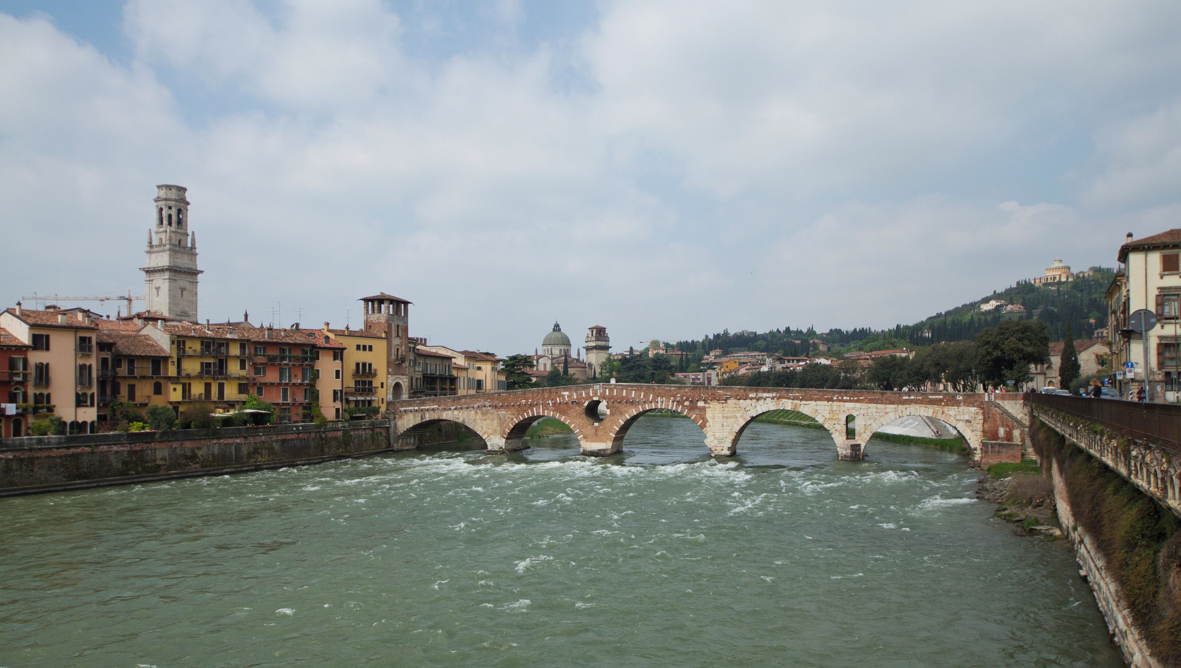 Un río con un puente de piedra, edificios históricos y una torre al fondo.