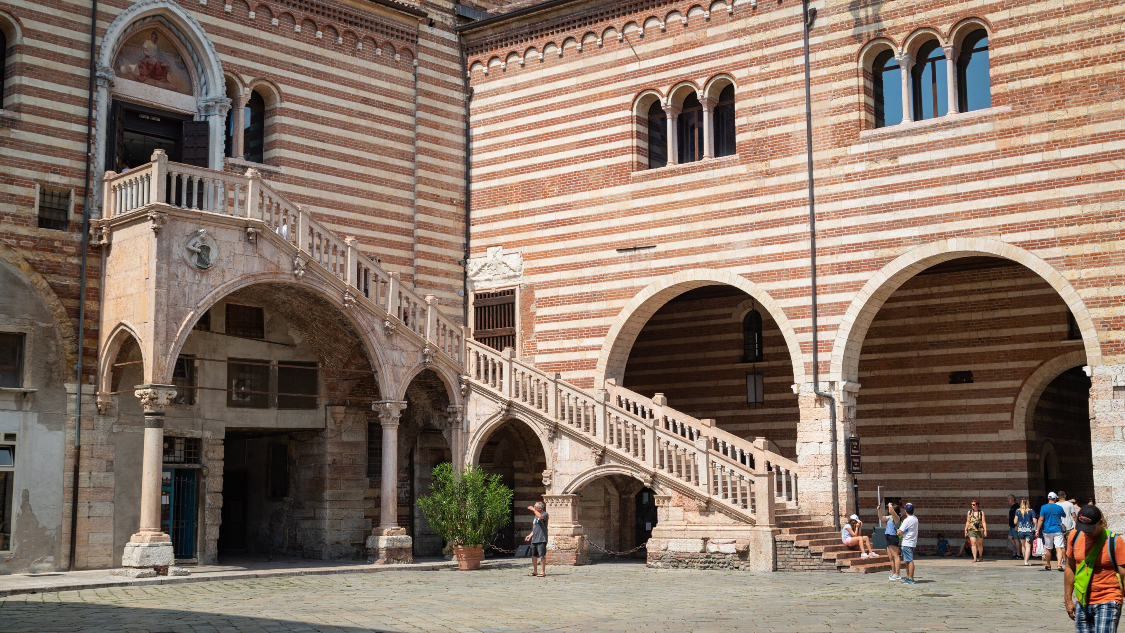 Un bâtiment historique aux murs en briques rayées, doté d’entrées en arc de cercle et d’un escalier central.