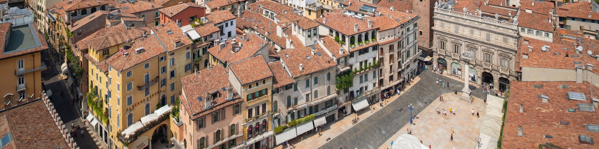 Una plaza histórica de la ciudad con tejados de tejas rojas, una torre destacada y una fuente.