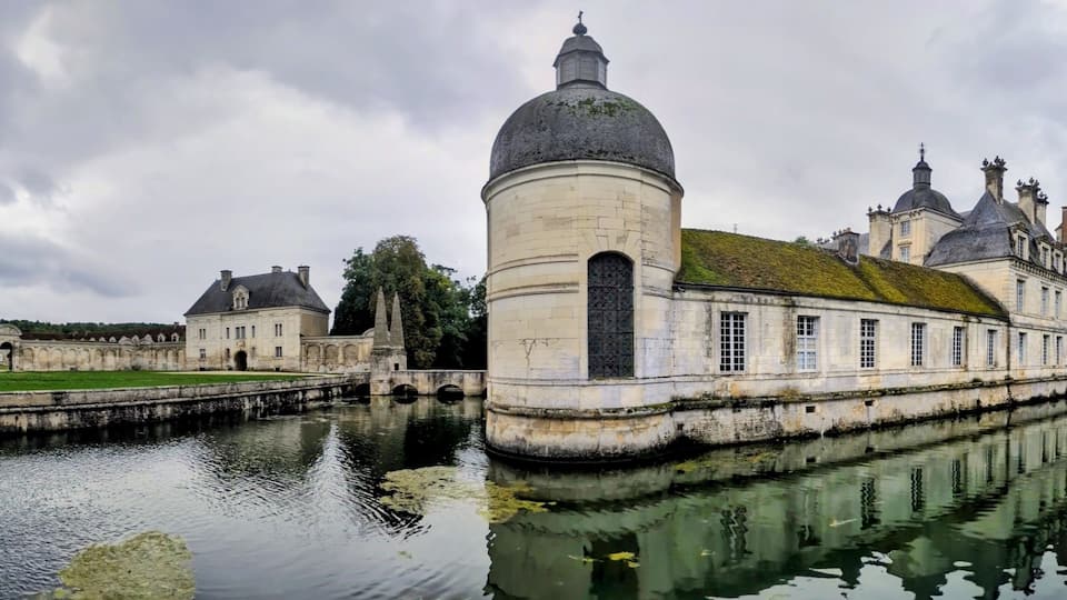 A historic building with a large dome and multiple towers, surrounded by a moat and greenery.