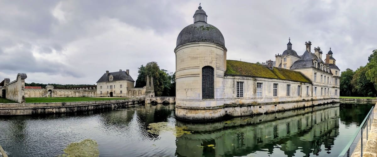 A historic building with a large dome and multiple towers, surrounded by a moat and greenery.