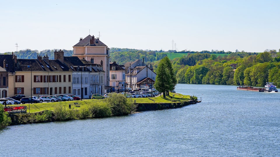 A river with a boat, a grassy bank, and buildings along the river.