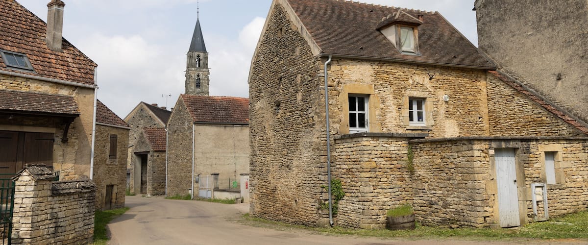 A narrow stone street flanked by old buildings with a church steeple in the background.