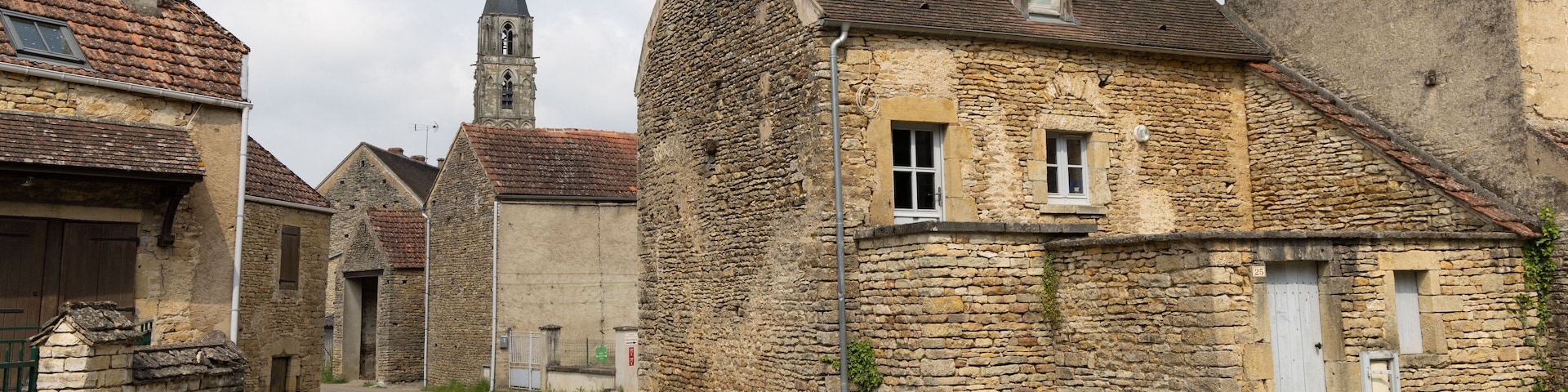 A narrow stone street flanked by old buildings with a church steeple in the background.