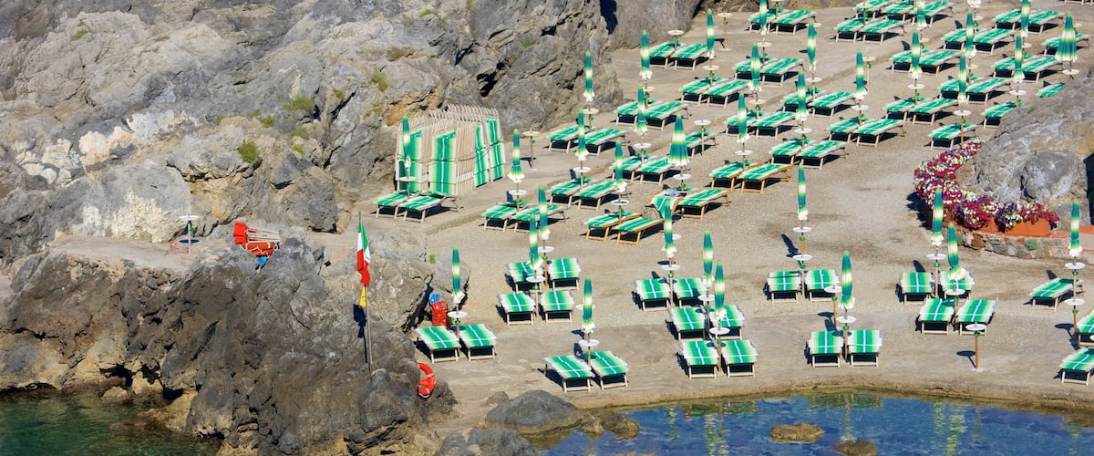 A rocky beach with rows of green lounge chairs and umbrellas.