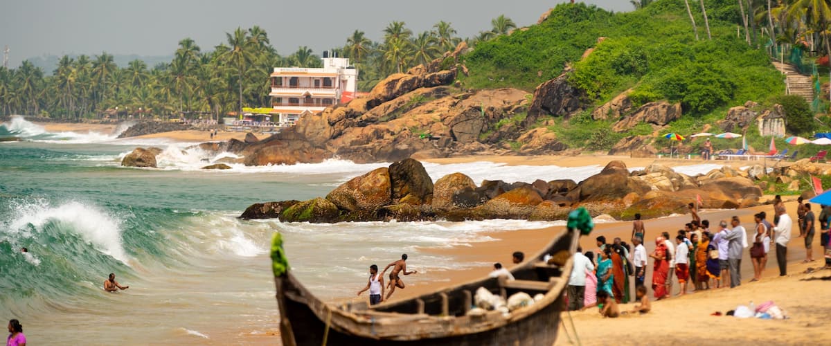 A beach with waves, people, and a boat.