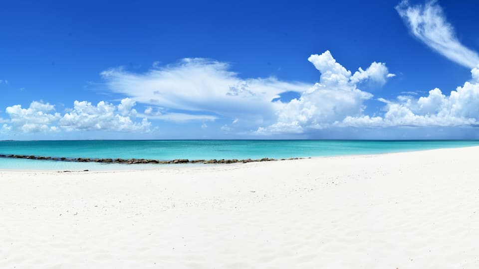 A white sandy beach with turquoise water and scattered clouds.