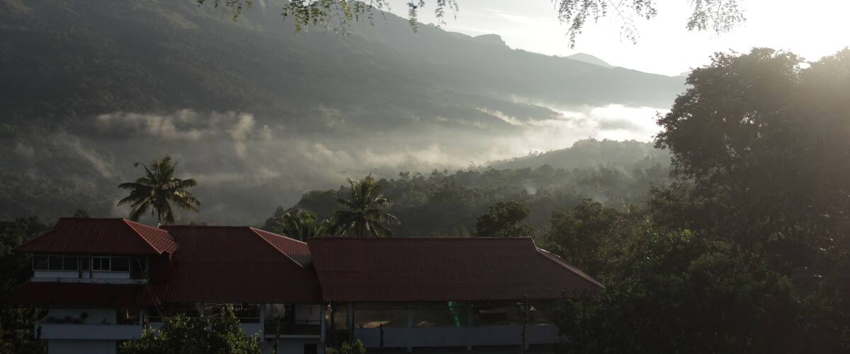 A mountainous landscape with a house and palm trees in the foreground.