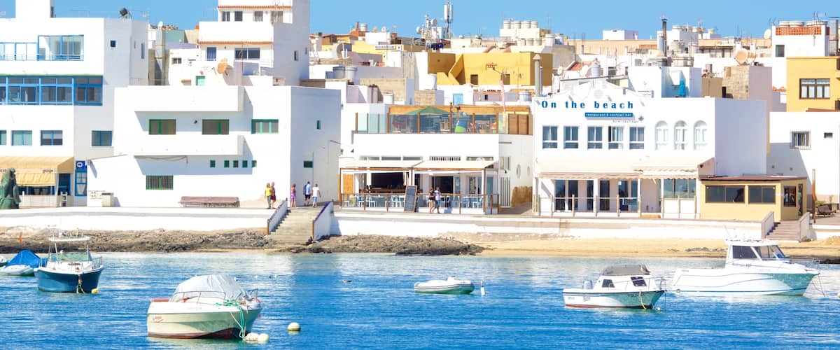 A coastal town with white and yellow buildings, a beach, and several boats anchored in the water.