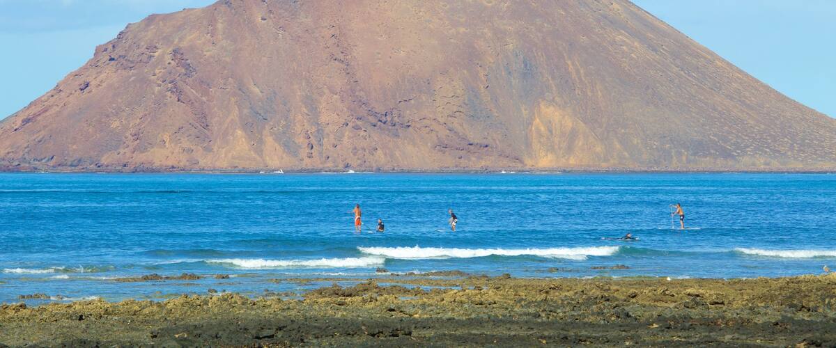 A mountain by the sea with people surfing.