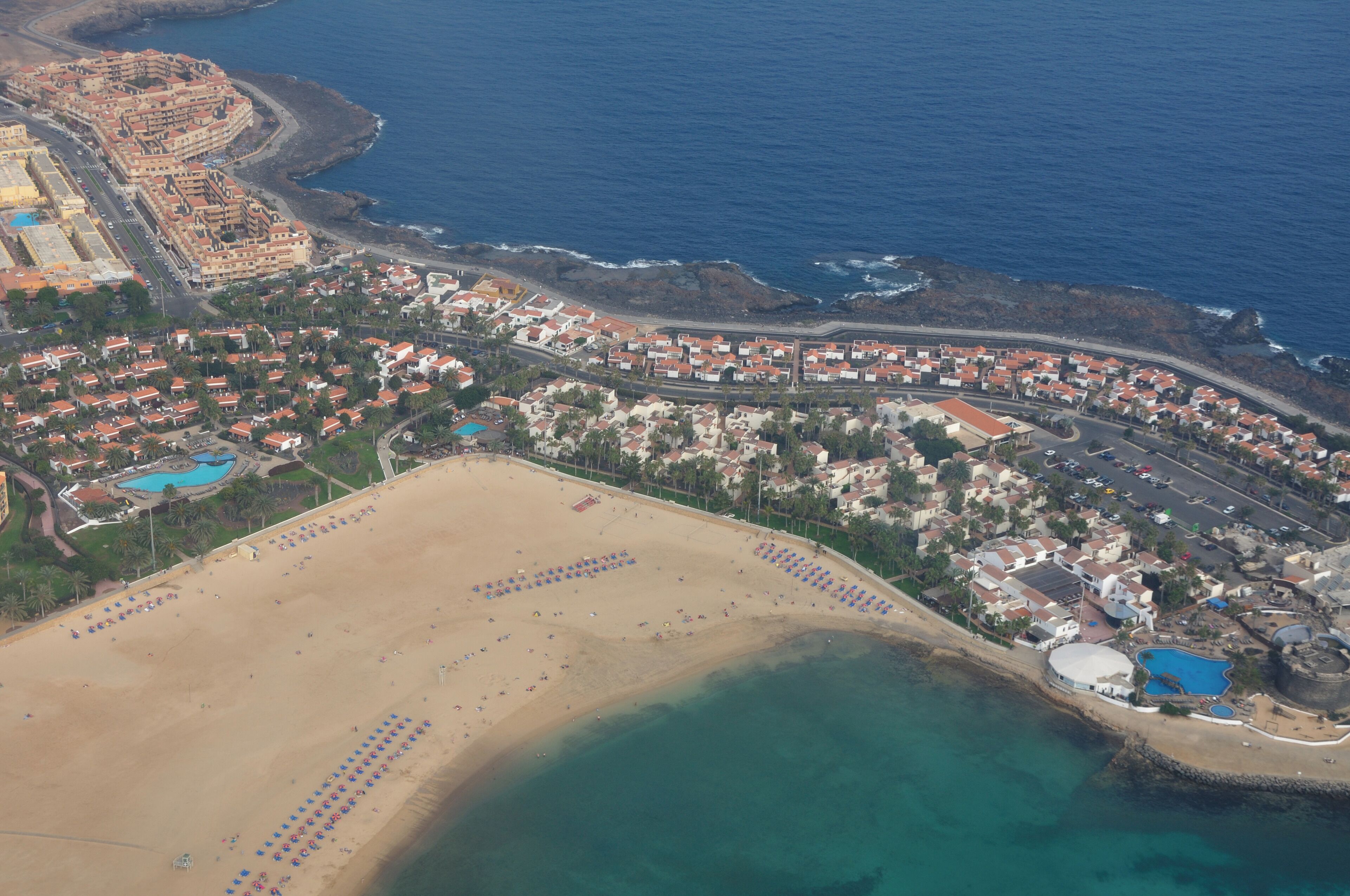 Eine Luftaufnahme einer Küstenstadt mit Strand, Wohngebieten und einer großen Wasserfläche.