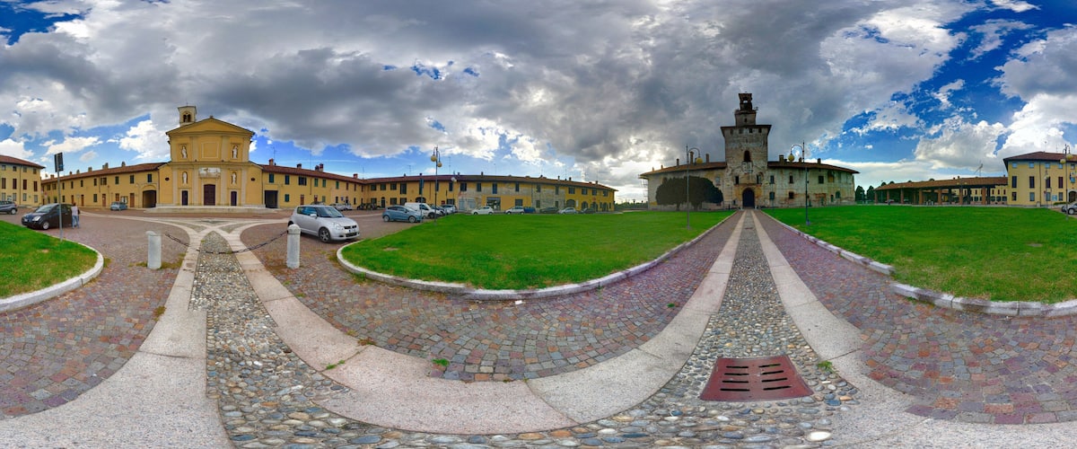 A historic plaza with a central fountain, surrounded by classical architecture and a cobblestone pathway.