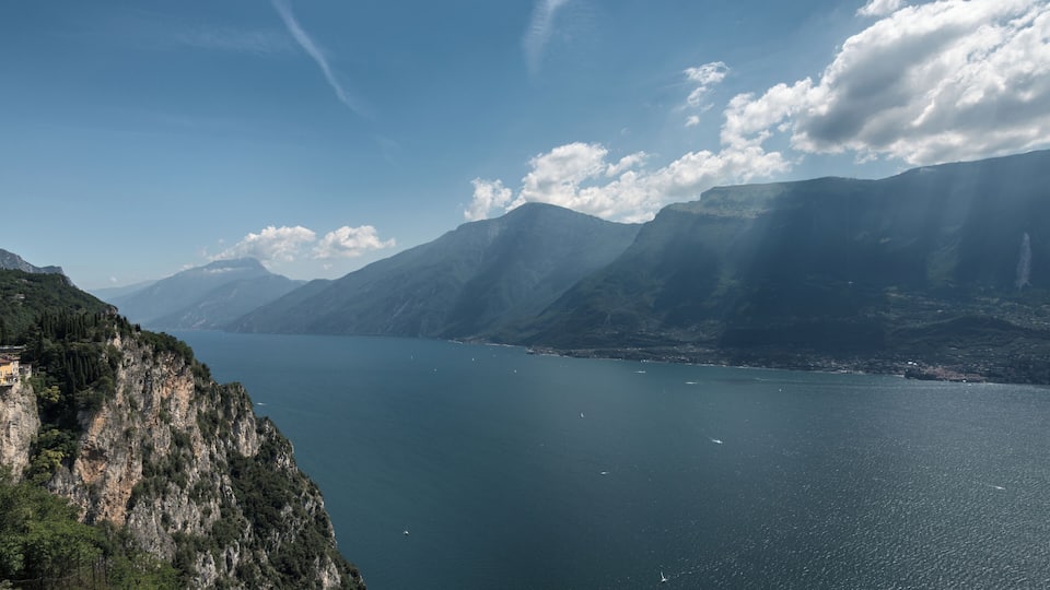 A mountainous landscape with a large body of water, likely a lake, surrounded by steep cliffs and distant mountains.