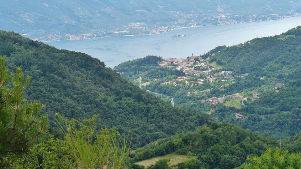 A mountainous landscape with a town nestled in the valley, a winding river, and a large body of water in the distance.