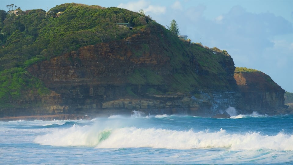 A coastal landscape with a rocky cliff and waves crashing against it.