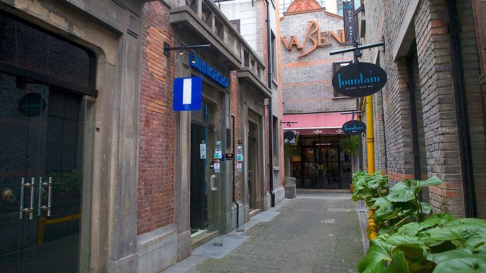 A narrow alley with brick buildings, a blue sign for a workshop, and a 'fountain' sign indicating a wine bar.