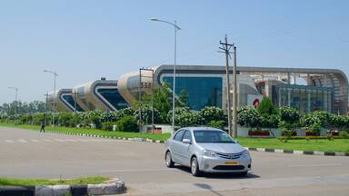 A modern building with a curved glass facade, a silver car parked in front, and a pedestrian crossing the road.