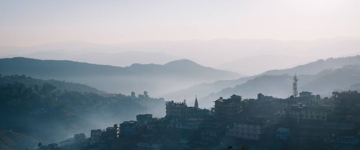 A misty mountain village with terraced houses and a prominent church spire.