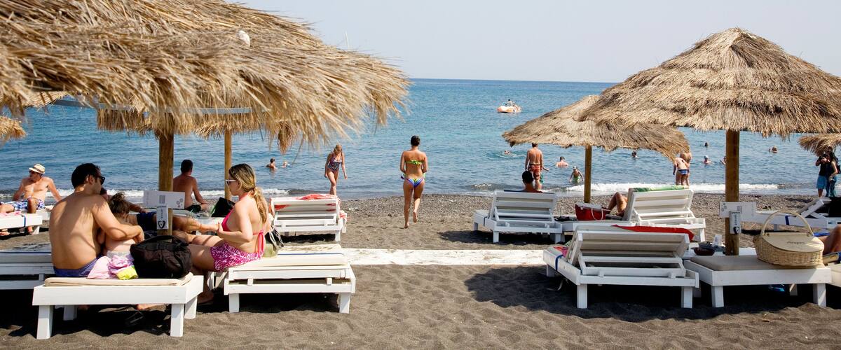 A beach with thatched umbrellas, sun loungers, and people swimming in the water.