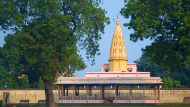 A temple with a tall spire, surrounded by trees and a pavilion.