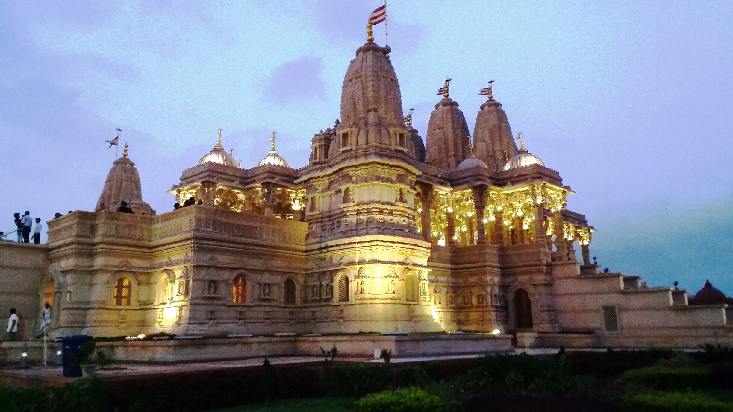 A large, illuminated temple with multiple spires and domes, featuring intricate carvings and a flag on top.