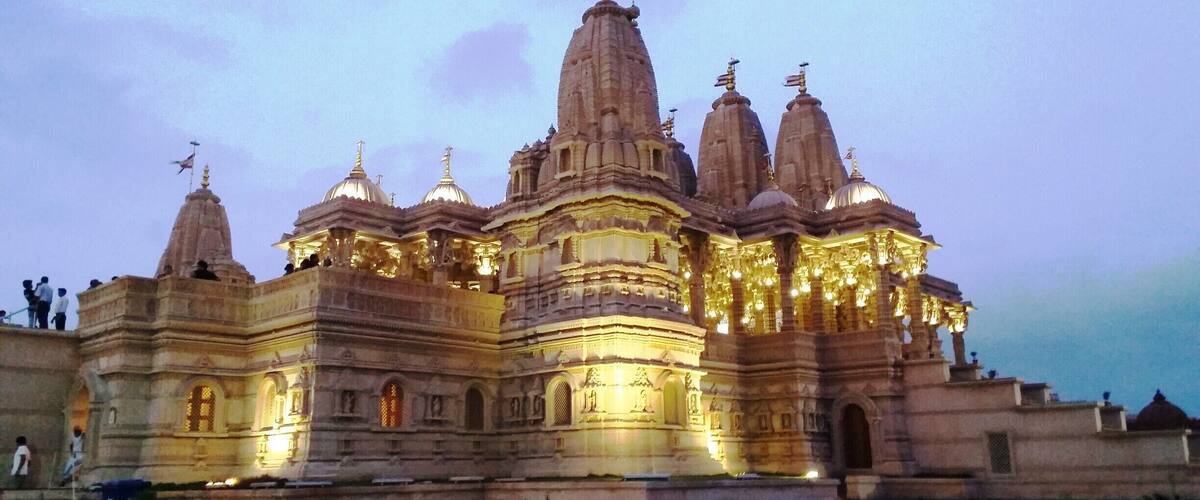 A large, illuminated temple with multiple spires and domes, featuring intricate carvings and a flag on top.
