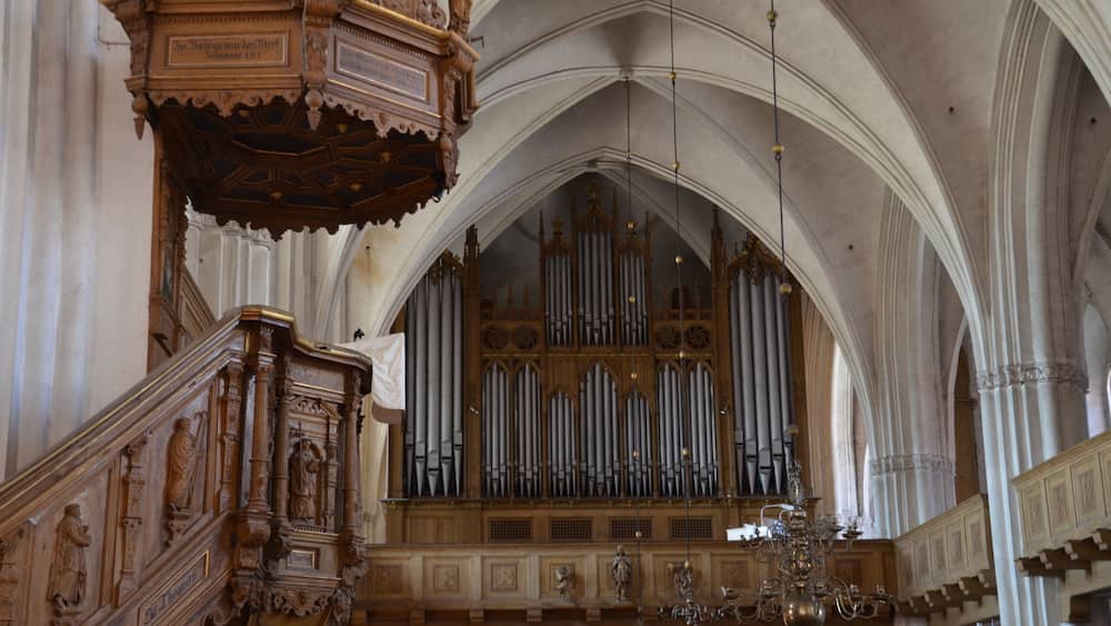 Eine kunstvoll gestaltete Orgel mit mehreren Pfeifen, ein hölzernes Pult und eine Chandelüster in einer Kathedrale.