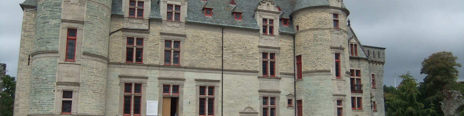 Un gran edificio de piedra histórico con múltiples torres y ventanas de marco rojo.