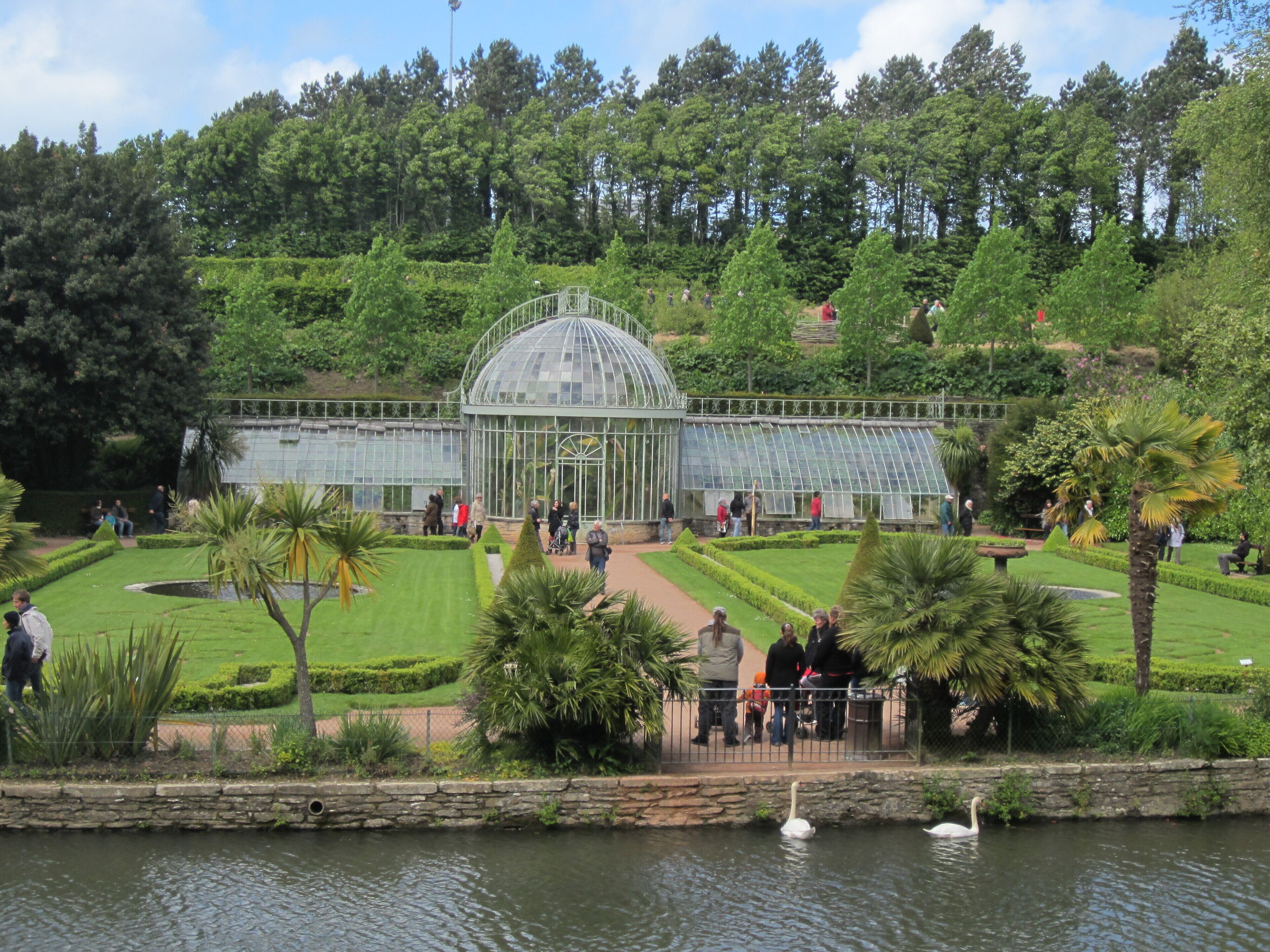 A greenhouse surrounded by manicured gardens and a pond with swans.