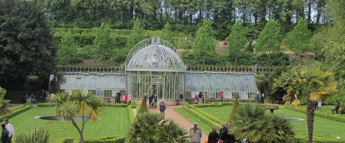 A greenhouse surrounded by manicured gardens and a pond with swans.