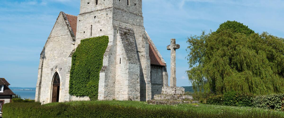 A historic stone church with a steep roof and a cross in front.