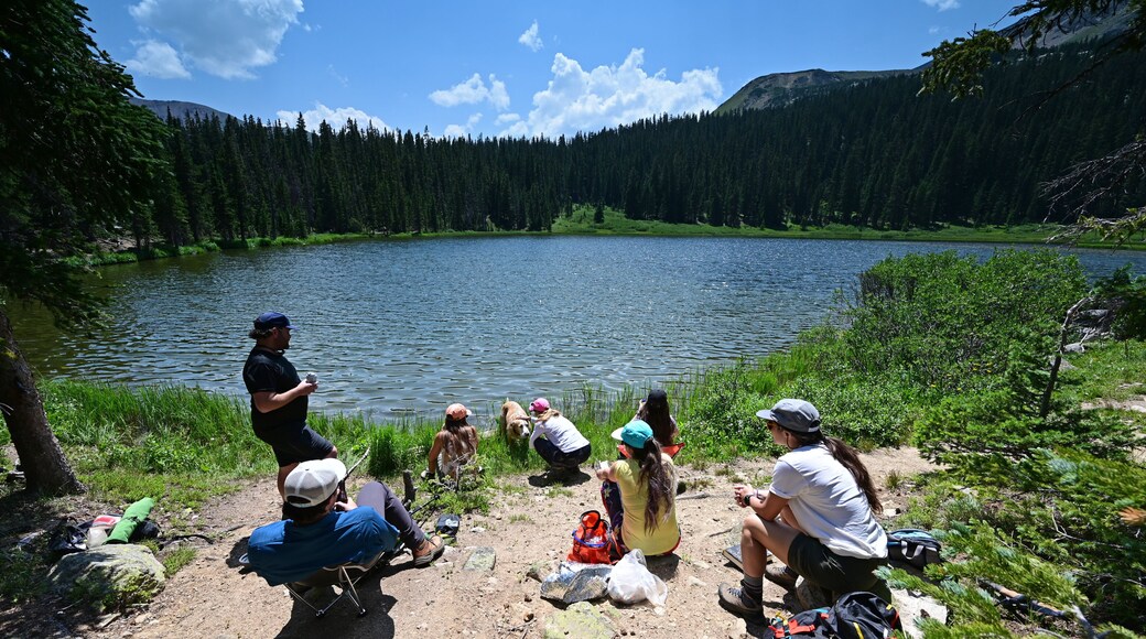 Hikers enjoy view of Hassell Lake in Arapaho National Forest, Colorado on sunny summer afternoon.