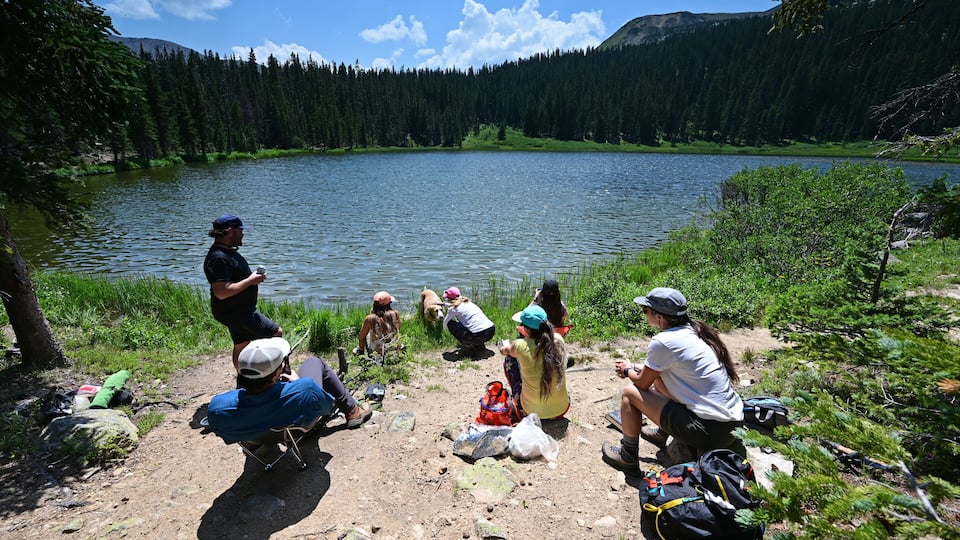 Hikers enjoy view of Hassell Lake in Arapaho National Forest, Colorado on sunny summer afternoon.