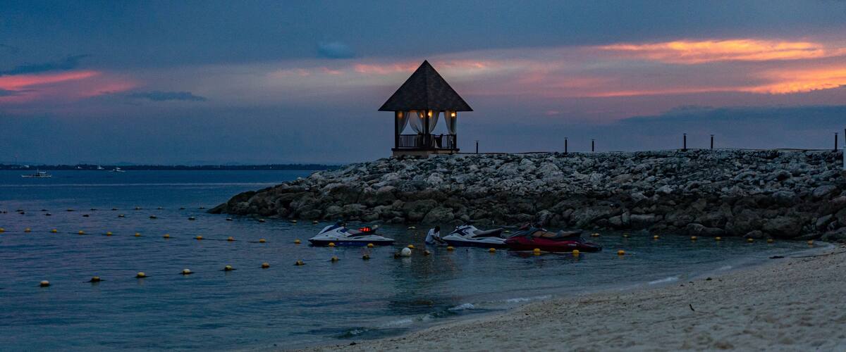 A beach with a gazebo, rocky shore, and boats.