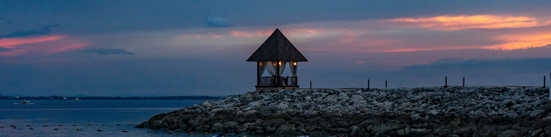 A beach with a gazebo, rocky shore, and boats.