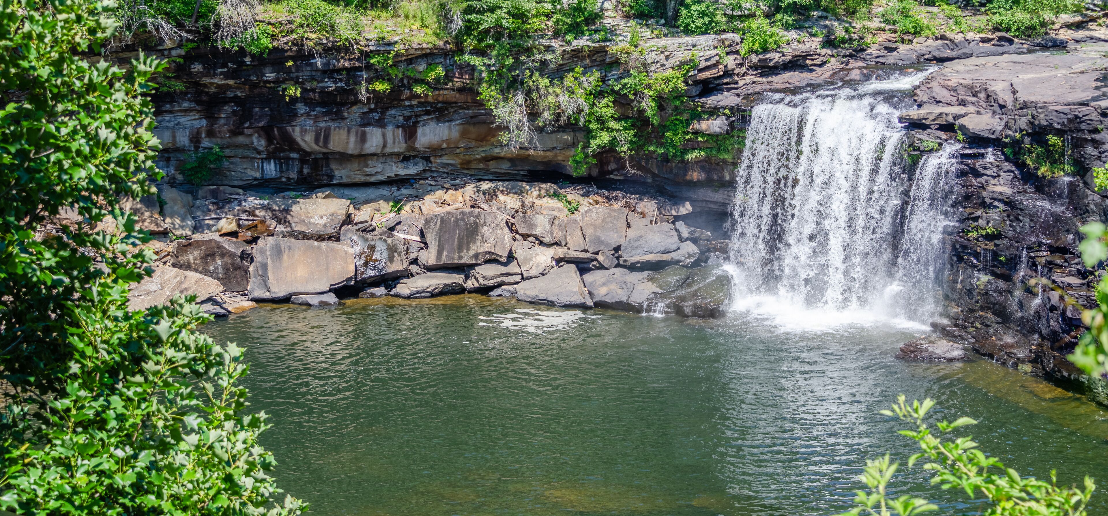 A waterfall cascading over rocky terrain into a clear pool surrounded by lush greenery.