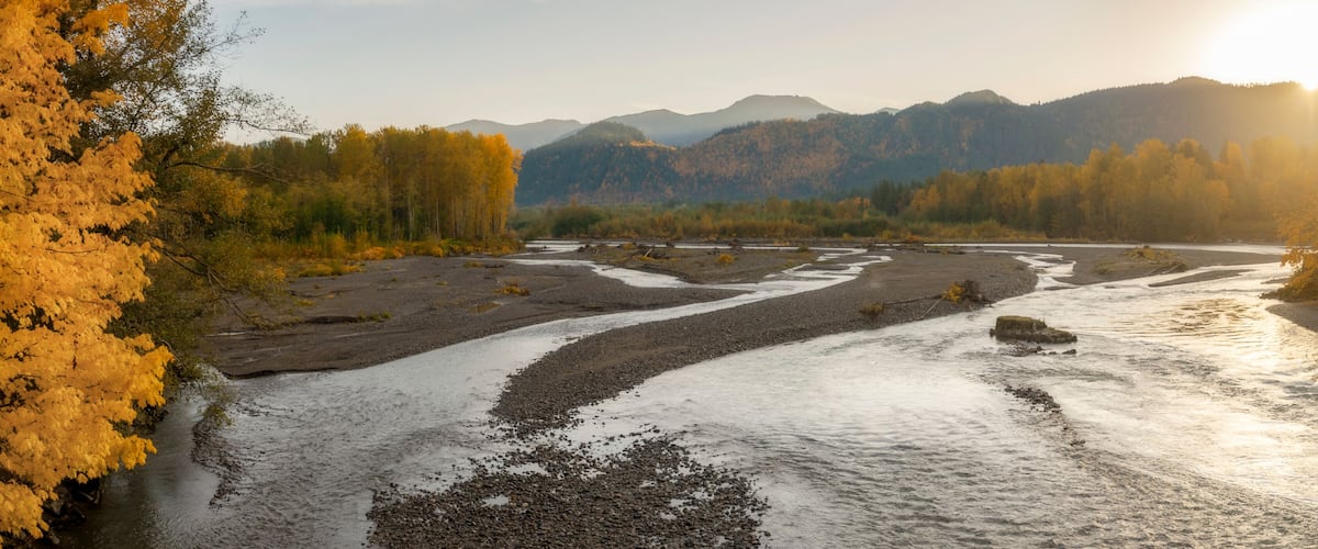 A river flowing through a valley with autumn-colored trees and mountains in the background.