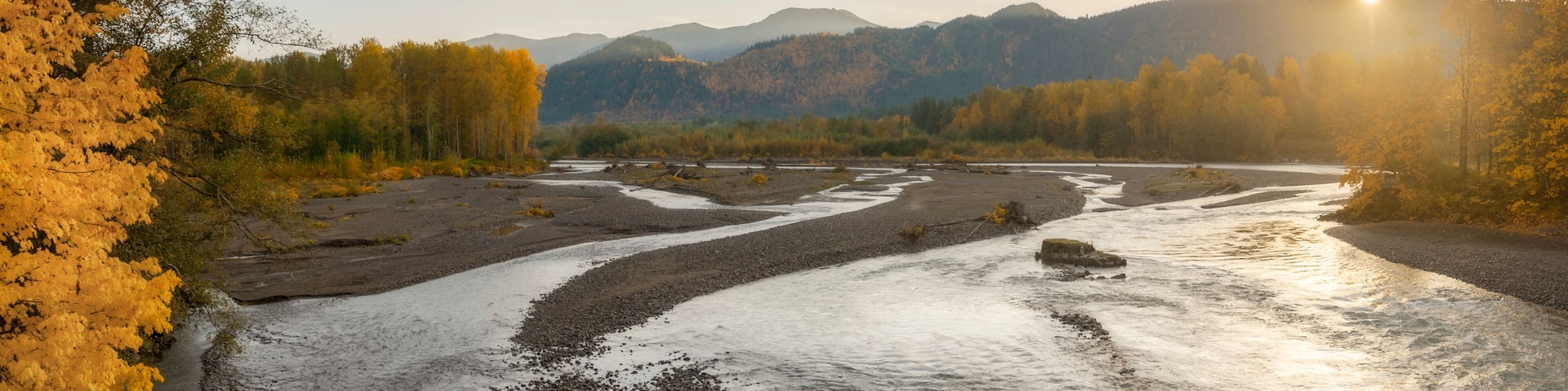 A river flowing through a valley with autumn-colored trees and mountains in the background.