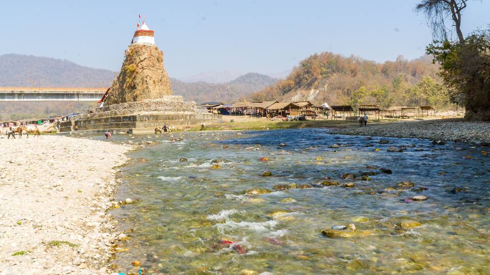 A river with clear water, a rocky shore, a bridge, and a mountain with a temple.