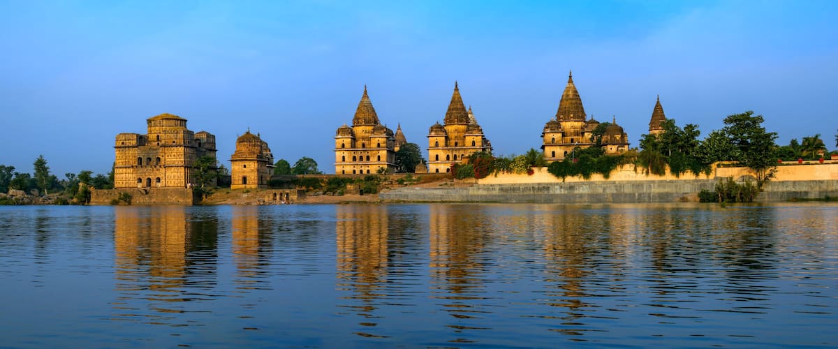 A historic temple complex with multiple spires and domes, situated by a calm river.