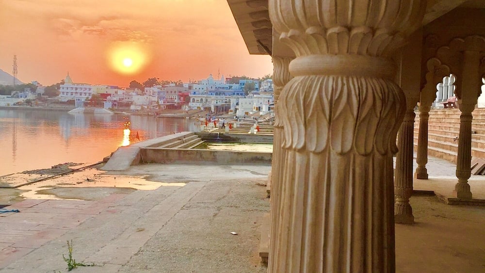 A sunset over a cityscape with a river, featuring classical architecture and a prominent column.
