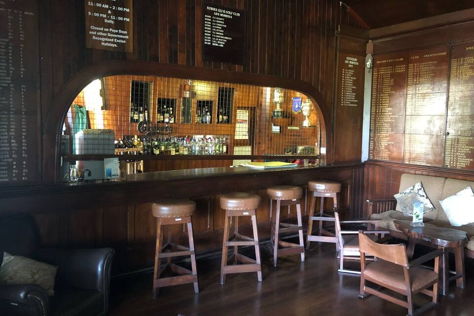 Um bar com painéis de madeira, balcão, banquetes e uma área de estar com sofá e cadeiras.