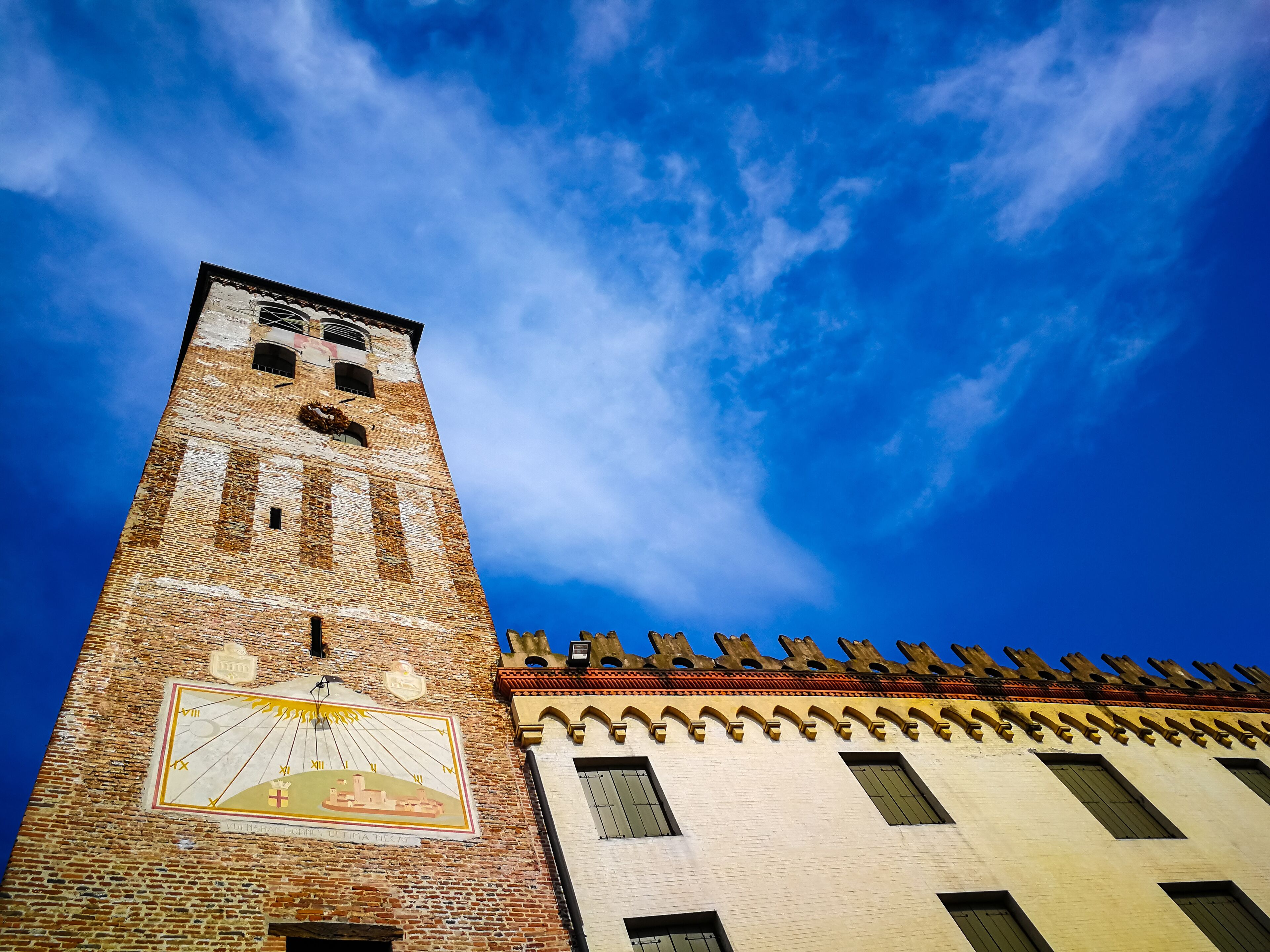 A tall brick tower with a clock and a mural, under a clear blue sky.