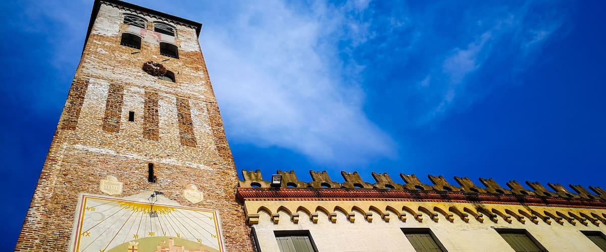 A tall brick tower with a clock and a mural, under a clear blue sky.