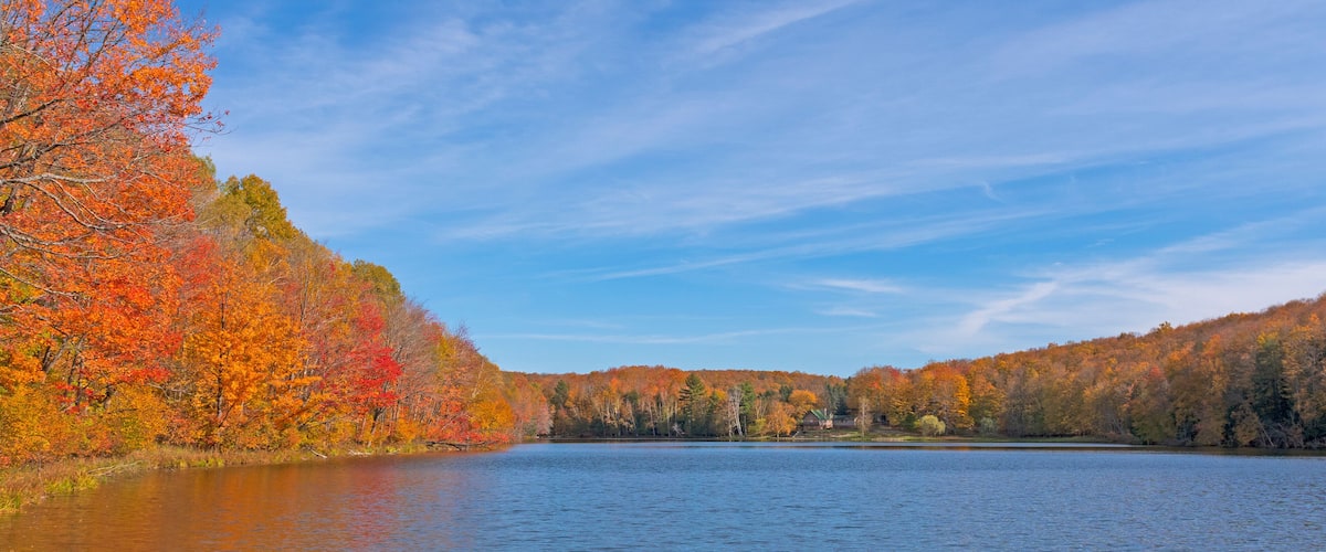 A lake surrounded by autumn-colored trees and a clear blue sky.