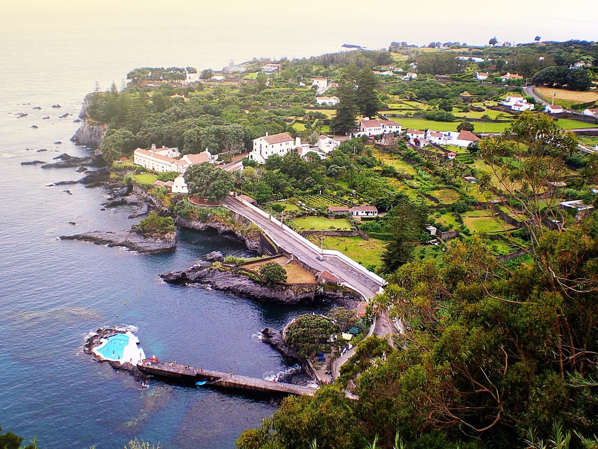A coastal town with a bridge, rocky coastline, and a swimming pool.