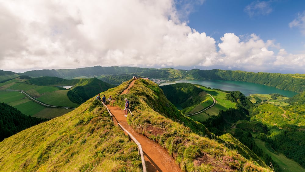A hiking trail on a grassy hill with a view of a lake and surrounding hills.